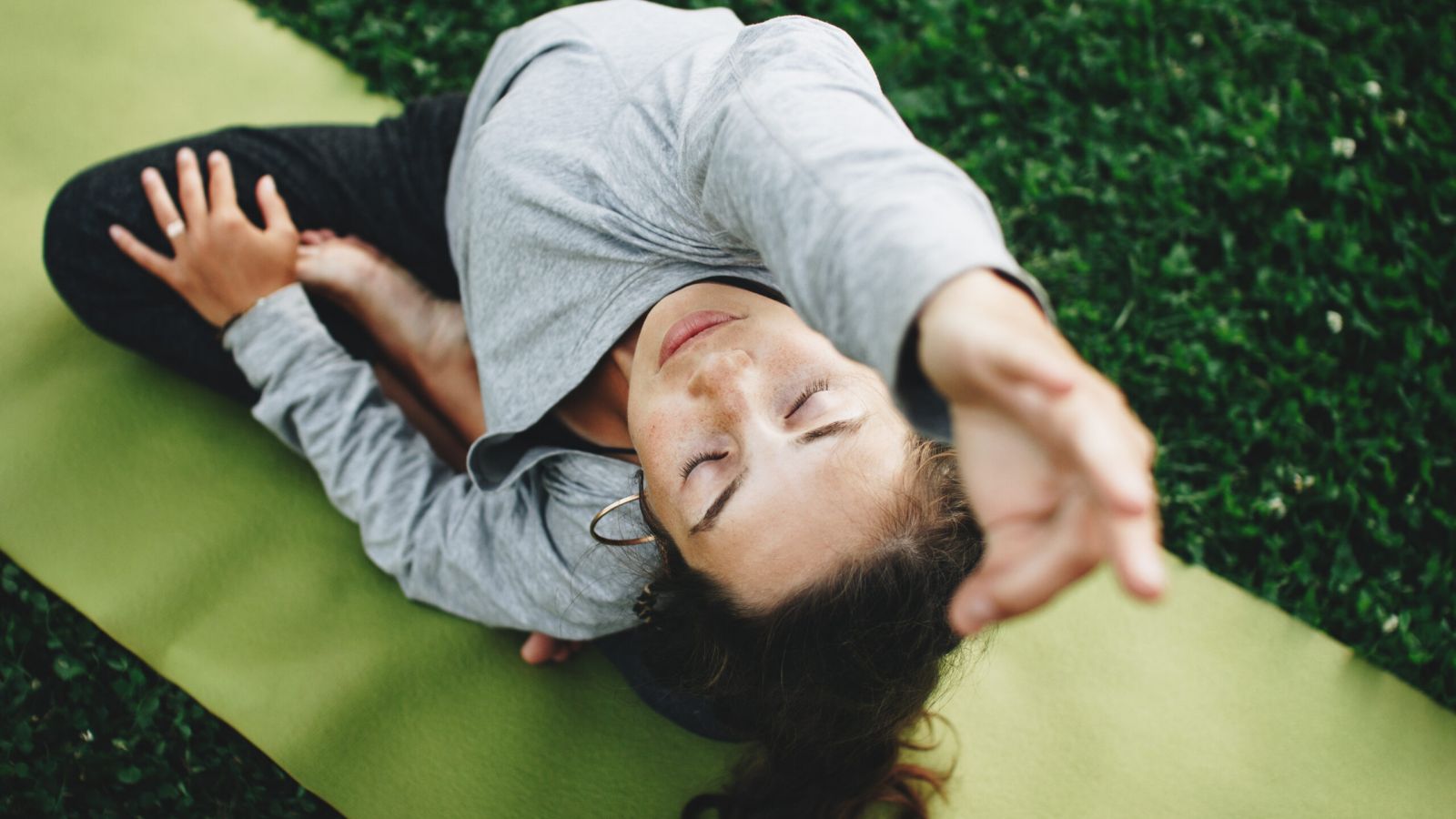 The Grove at Stone Park apartment homes with Woman practicing yoga outdoors on a green mat, stretching with eyes closed on a grassy surface.