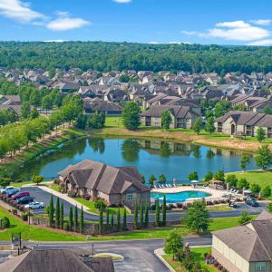 The Grove at Stone Park apartment homes with Aerial view of a suburban neighborhood with a central pond, swimming pool, and clubhouse surrounded by houses.