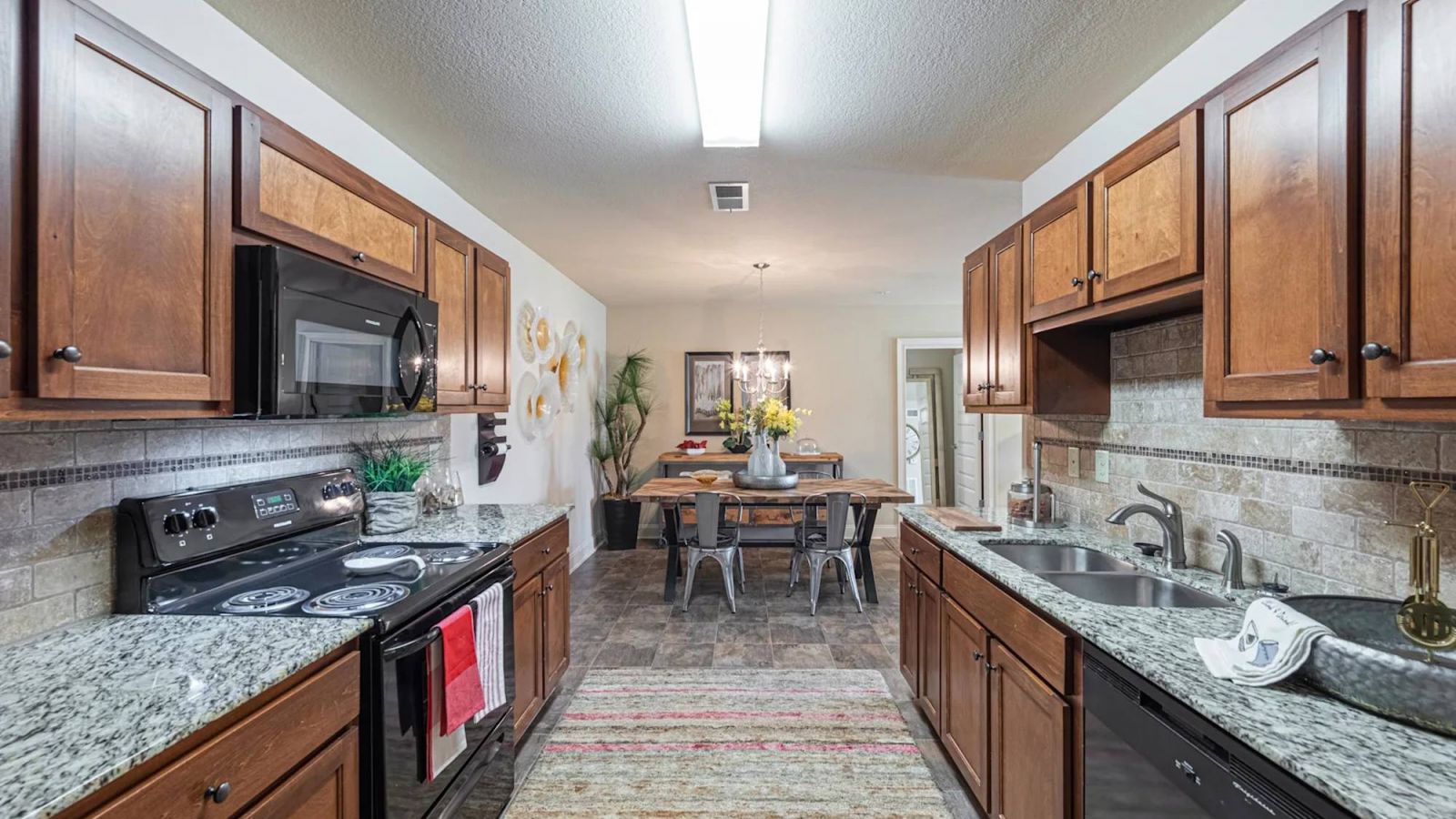 The Grove at Stone Park apartment homes with Modern kitchen with wooden cabinets, granite countertops, and view into a dining area with a table and chairs.