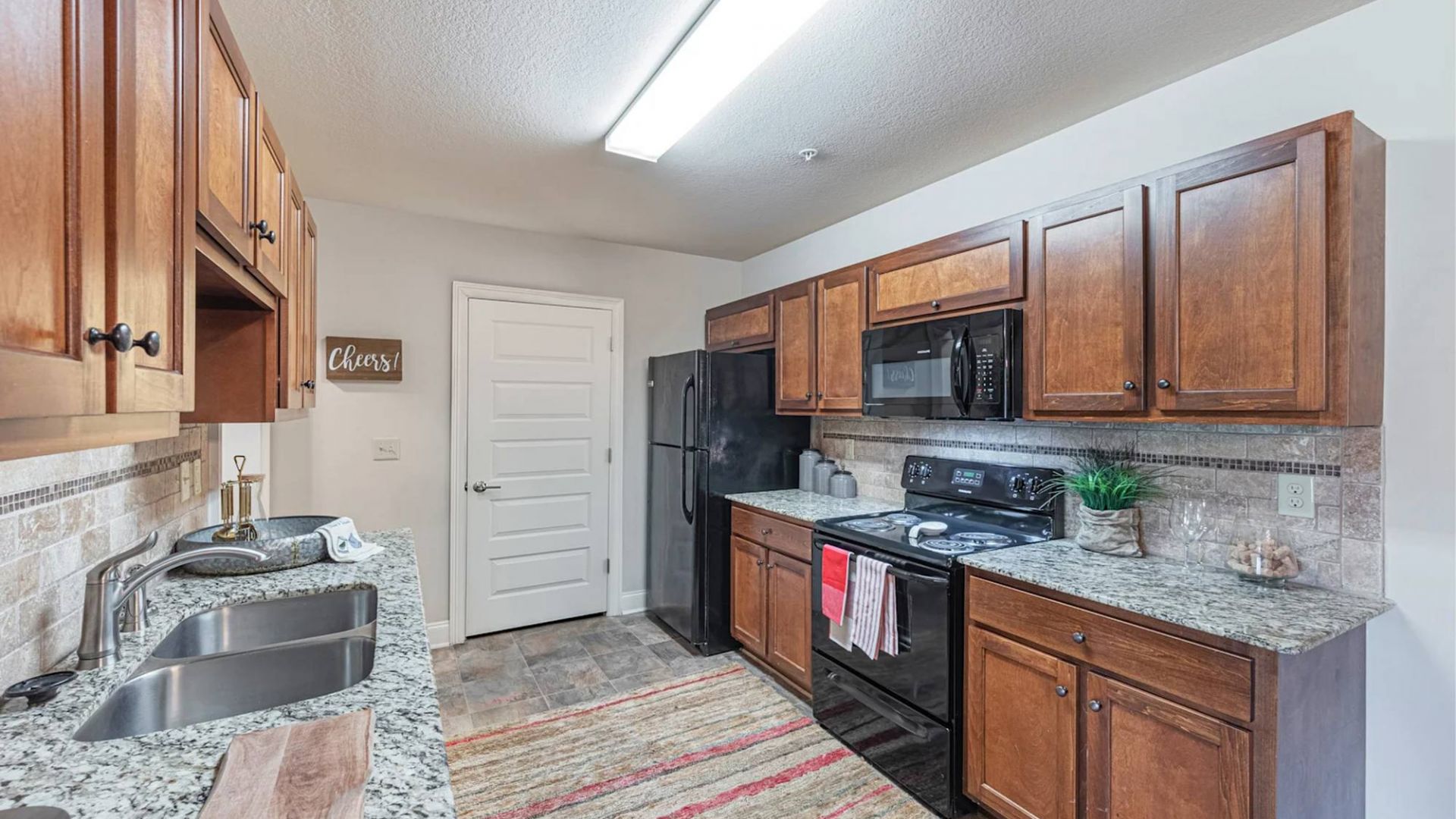 The Grove at Stone Park apartment homes with Modern kitchen with wooden cabinets, granite countertops, and stainless steel appliances under bright lighting.