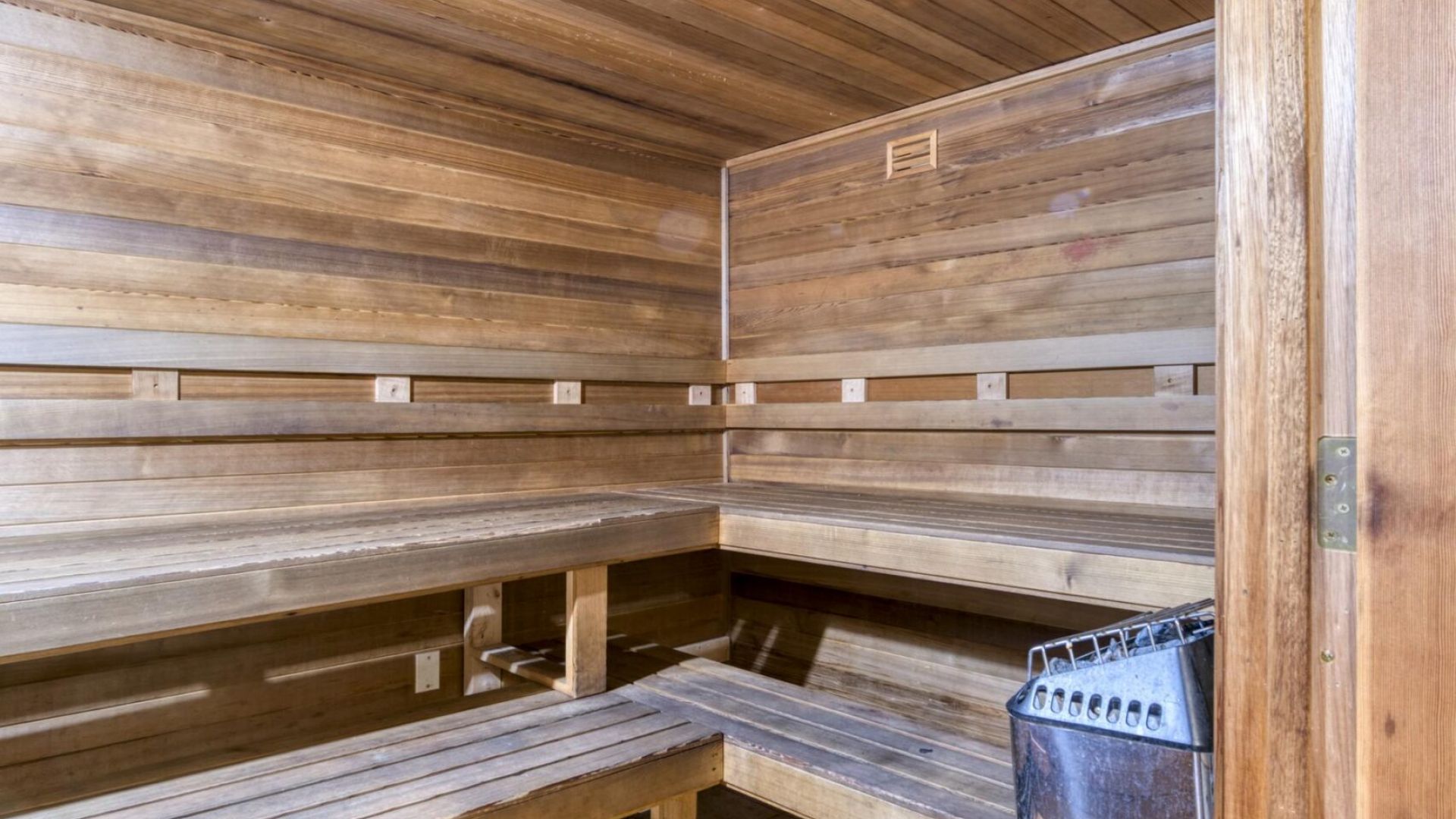 The Grove at Stone Park apartment homes with Wooden sauna interior with tiered benches and a metal heater in the corner, lit by a ceiling light.