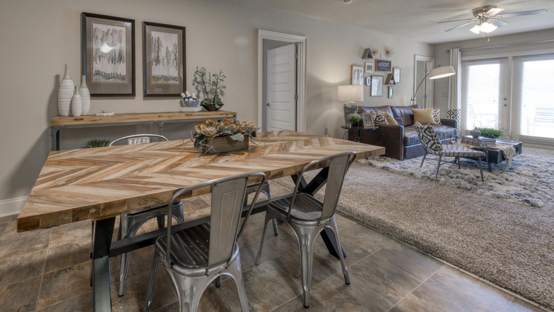 The Grove at Stone Park apartment homes with Modern dining and living area with chevron wood table, metal chairs, sofa, and large windows letting in natural light.