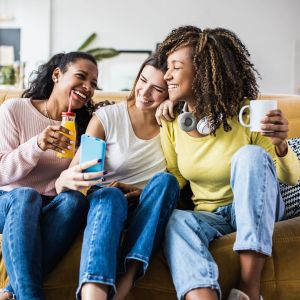 The Grove at Stone Park apartment homes with Three women sitting on a couch, laughing and taking a selfie together while holding drinks.