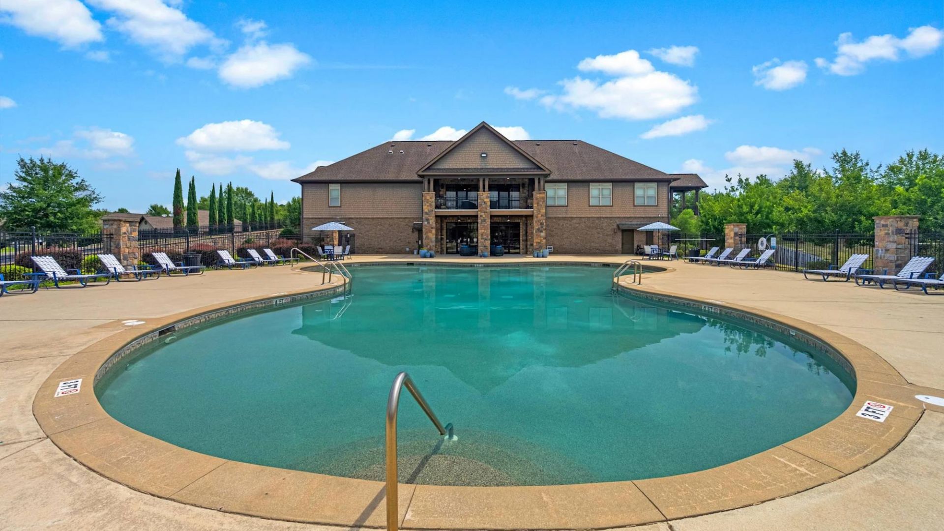 The Grove at Stone Park apartment homes with Large outdoor pool with clear water, lounge chairs, and a clubhouse building in the background under a blue sky.