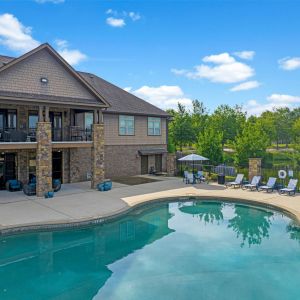 The Grove at Stone Park apartment homes with Large house with stone pillars beside a curved swimming pool, lounge chairs, and trees in the background.