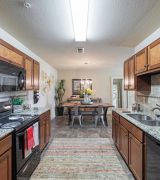 The Grove at Stone Park apartment homes with Modern kitchen with wood cabinets, granite countertops, and view into a dining area with a table and chairs.