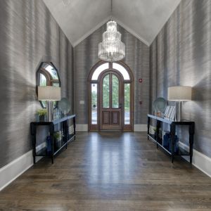 The Grove at Stone Park apartment homes with Elegant hallway with wood floors, a large chandelier, mirrors, and glass doors letting in natural light.