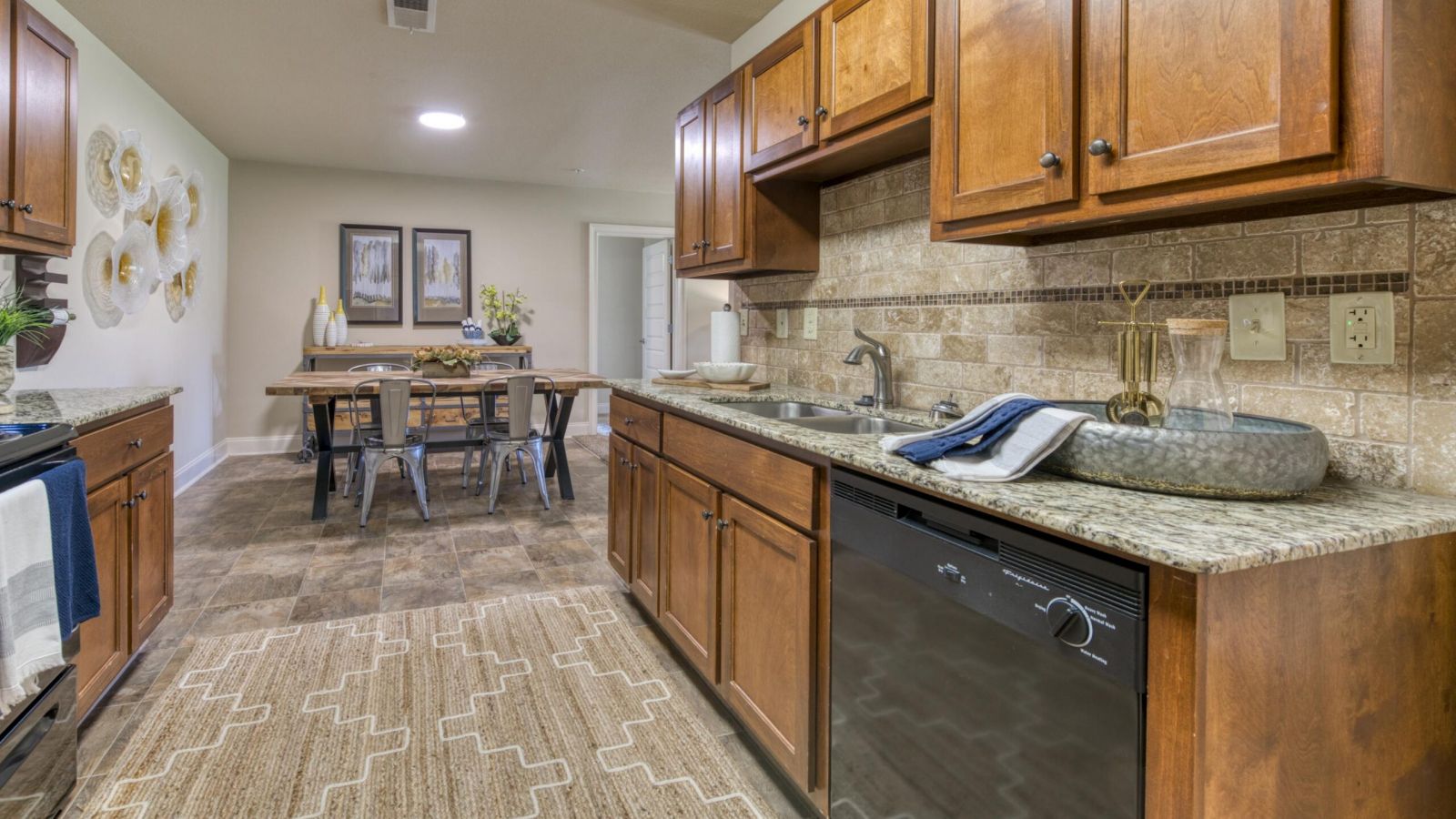The Grove at Stone Park apartment homes with Kitchen with brown cabinets, granite countertops, a rug, and a view of a dining table with chairs in the background.