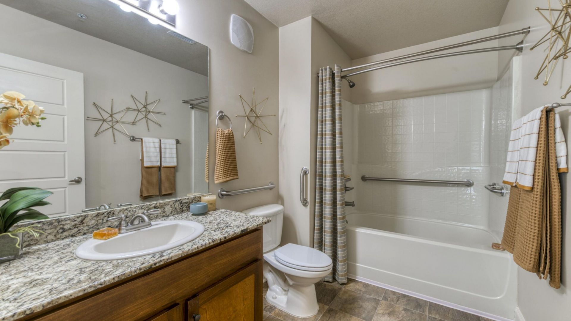 The Grove at Stone Park apartment homes with Modern bathroom with granite countertop, single sink, and white bathtub with safety bars, tan towels, and decorative wall art.