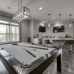 The Grove at Stone Park apartment homes with A modern game room with a pool table, bar stools, wall-mounted TVs, large windows, and pendant lights.